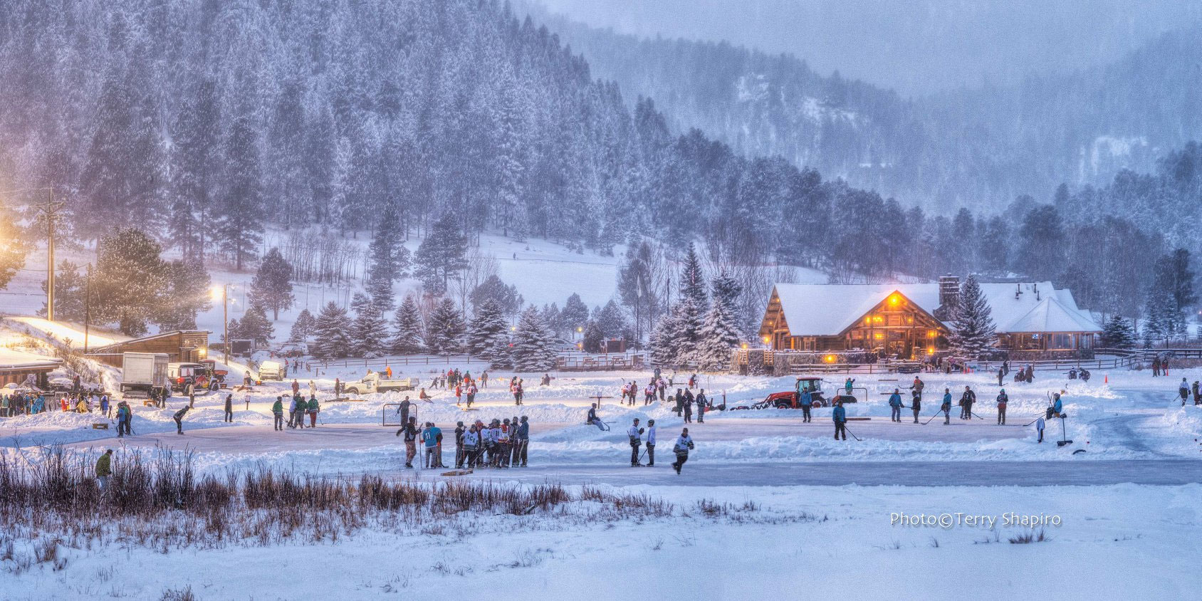 People ice skating on frozen lake in evergreen at dusk